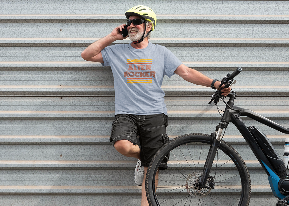 Man with a bicycle leaning against a metal wall, wearing a t-shirt and helmet.