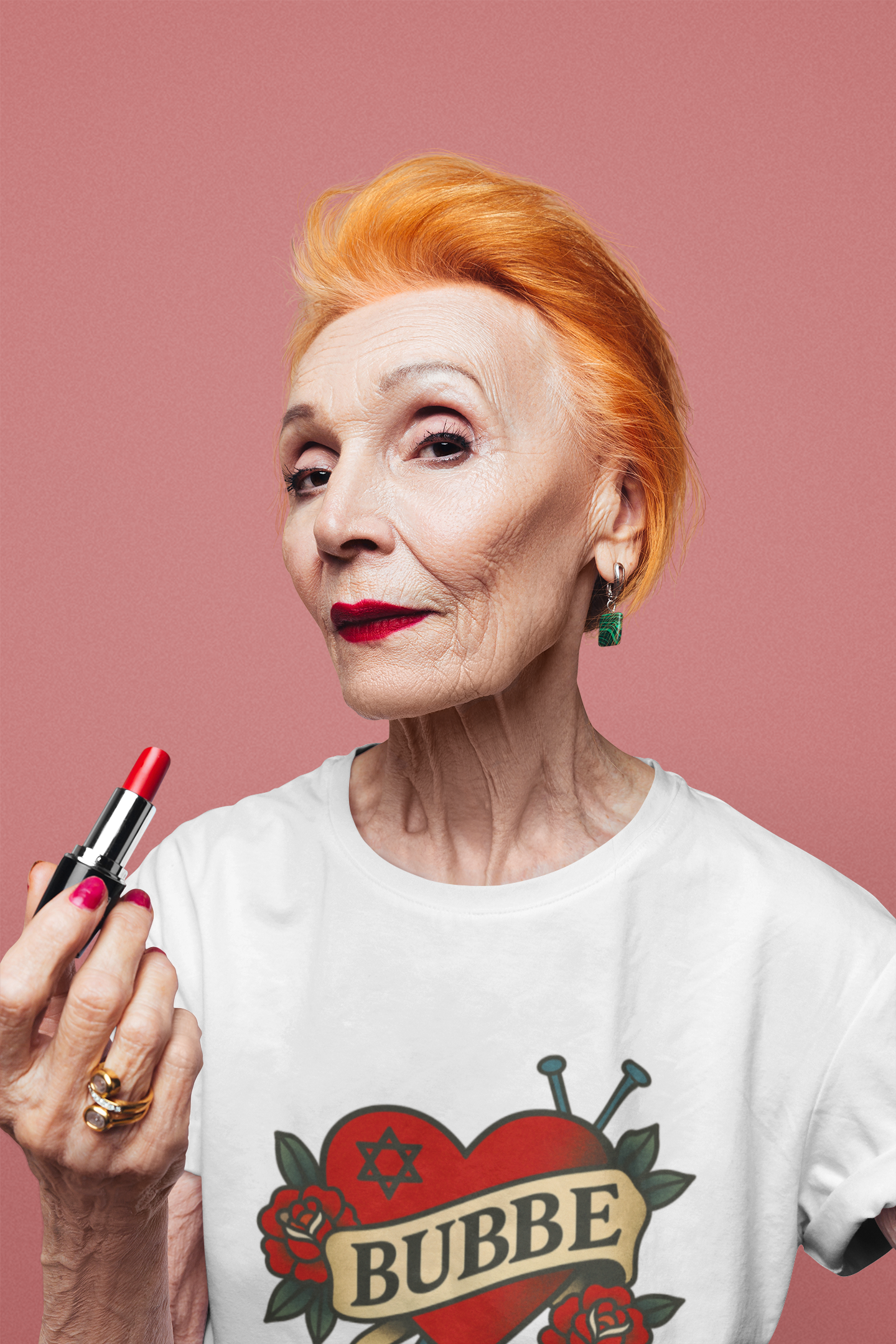 Woman holding a red lipstick with a white t-shirt featuring a heart design and the word 'BUBBE' on a pink background.