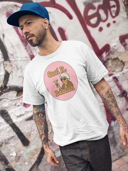 Man wearing a white t-shirt with a graphic design and text, standing against a graffiti-covered wall.