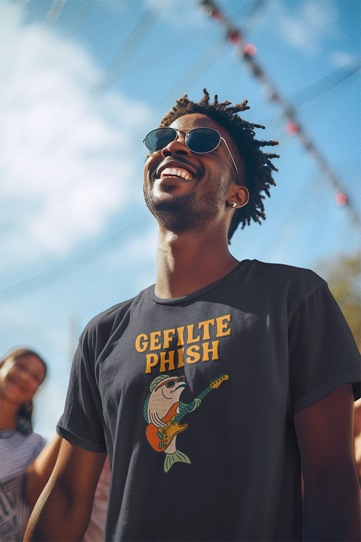 Man wearing a black t-shirt with 'Gefilte Phish' design, standing outdoors under a blue sky.