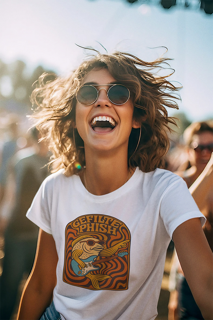 Person wearing a white t-shirt with a graphic design, smiling at an outdoor event.