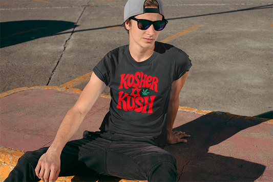 Person wearing a black t-shirt with 'Kosher Kush' text sitting on a concrete surface.