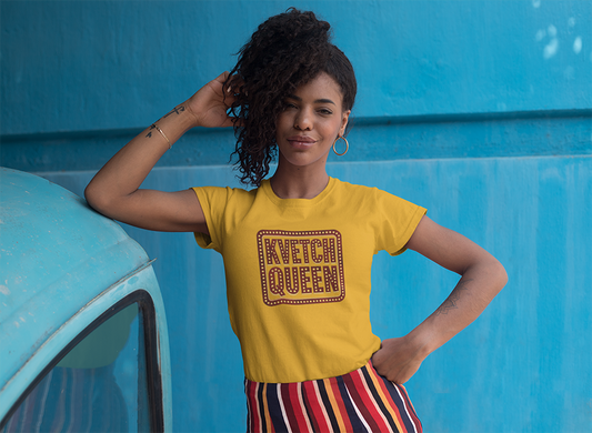 Woman wearing a yellow t-shirt with 'KVETCH QUEEN' text against a blue wall.