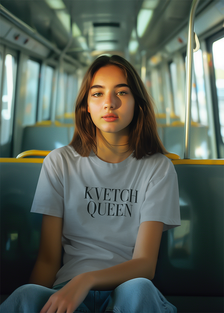 Person wearing a white t-shirt with 'KVETCH QUEEN' text on a bus.