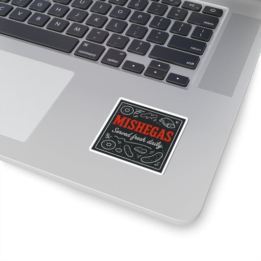 Laptop with a sticker that reads 'Mishegas Served fresh daily' on a white background