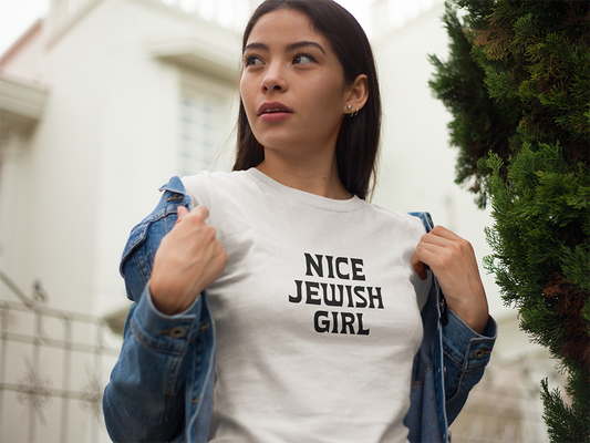 Woman wearing a white t-shirt with 'Nice Jewish Girl' text outdoors.