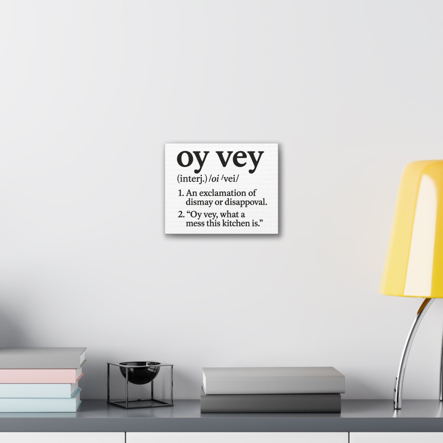 Decorative wall art with the word 'oy vey' definition on a white wall above a shelf.