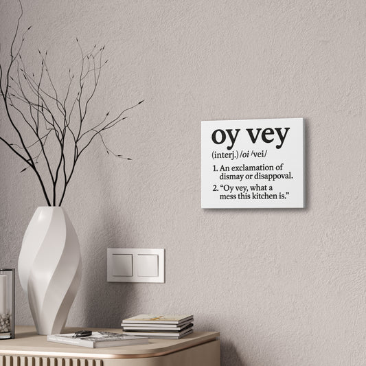 Decorative wall sign with the word 'oy vey' definition on a neutral wall with a vase and books.