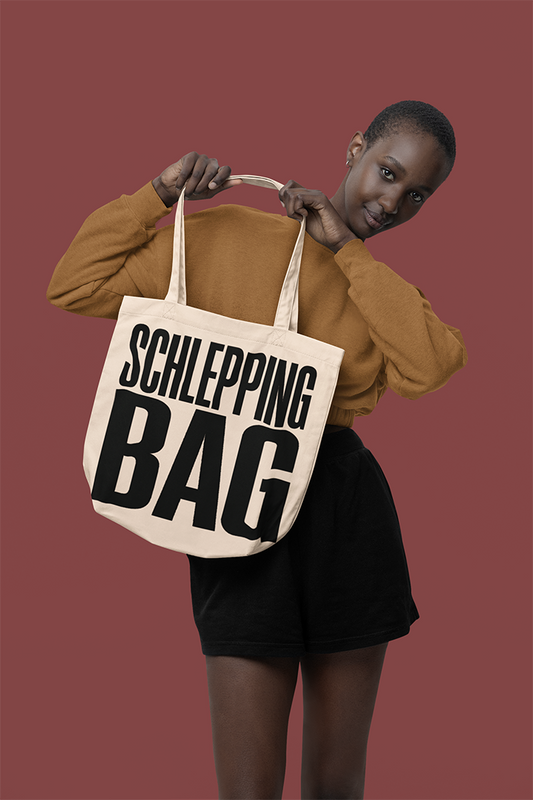 Person holding a tote bag with 'SCHLEPPING BAG' text against a red background
