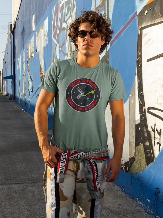 Person wearing a green t-shirt with a graphic design in front of a graffiti-covered wall.