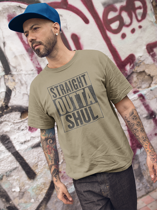 Man wearing a green t-shirt with text and a blue cap in front of a graffiti-covered wall.