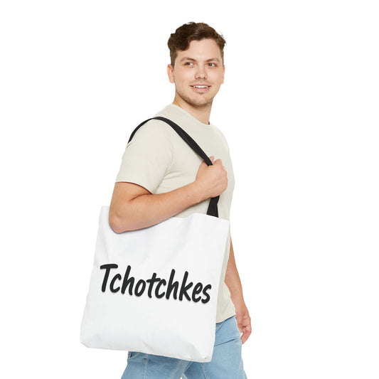 Man holding a white tote bag with 'Tchotchkes' text on a white background