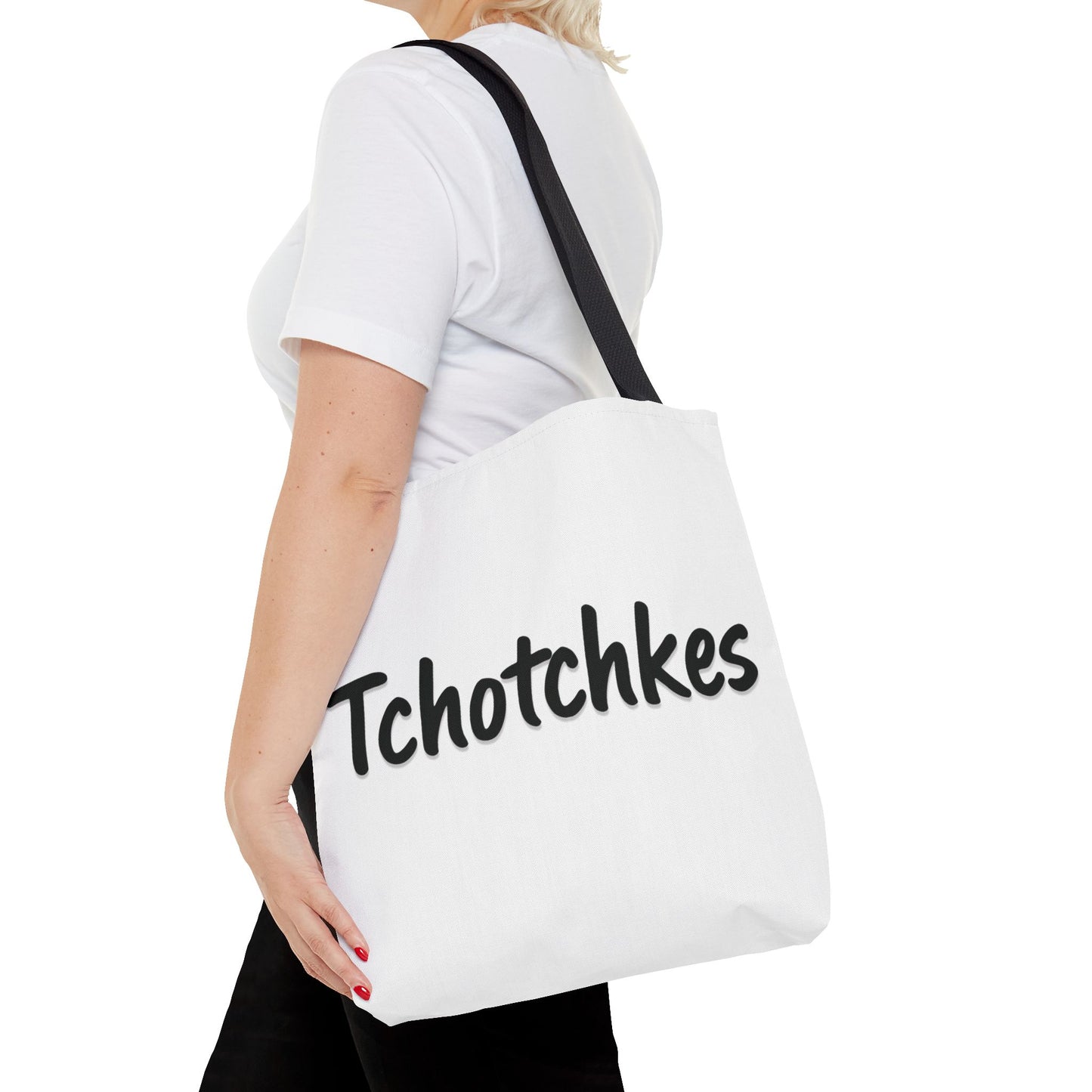 Person holding a white tote bag with 'Tchotchkes' text on a white background