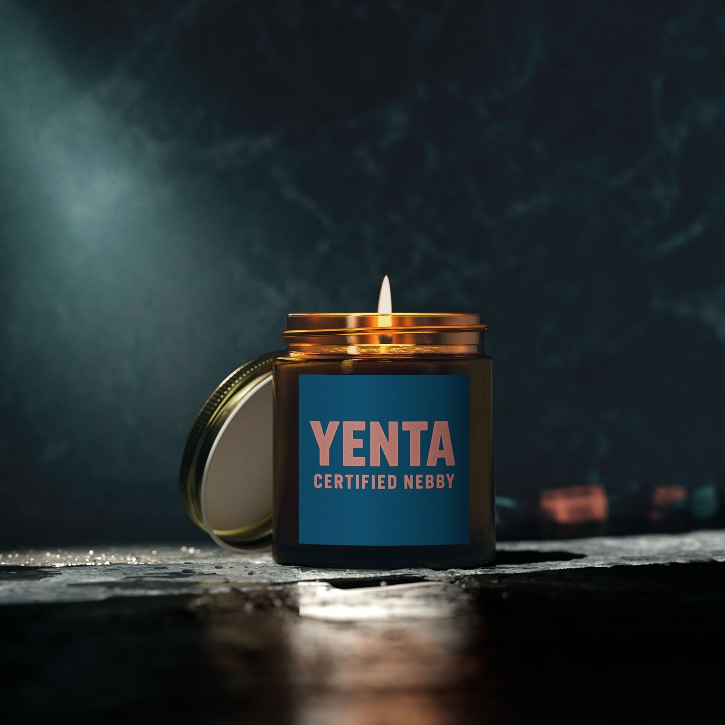 Candle in a jar labeled 'Yenta Certified Nebby' on a dark background