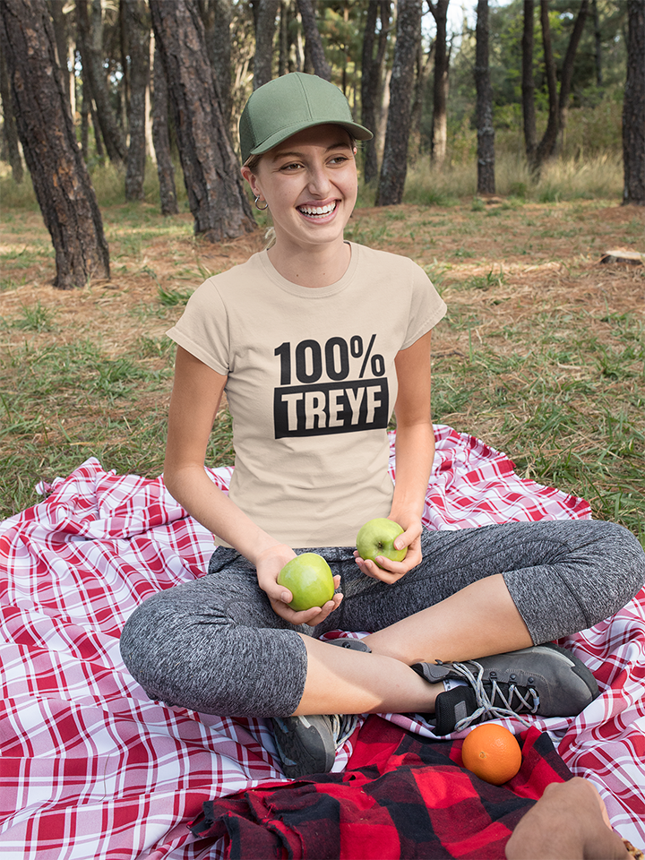 Person sitting on a red and white checkered blanket in a forest, wearing a '100% TREYF' t-shirt.