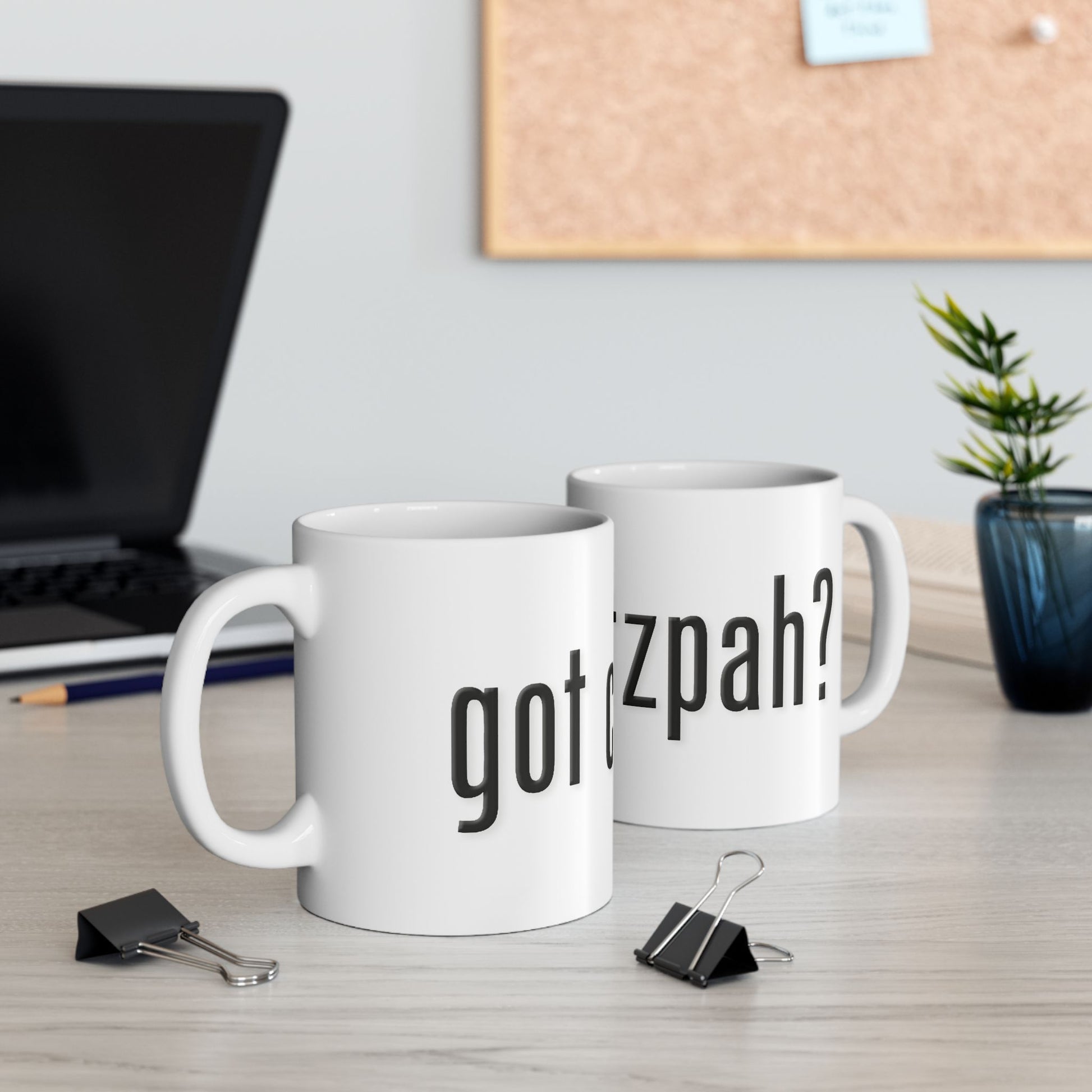Two white mugs with text 'got chutzpah?' on a desk with office supplies and a plant.