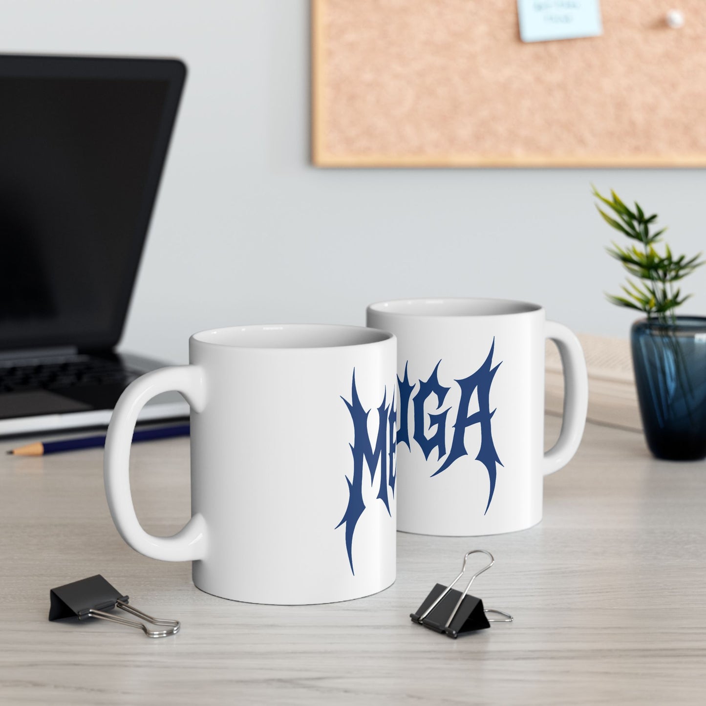 Two white mugs with blue 'meshuga' design on a desk with office supplies.