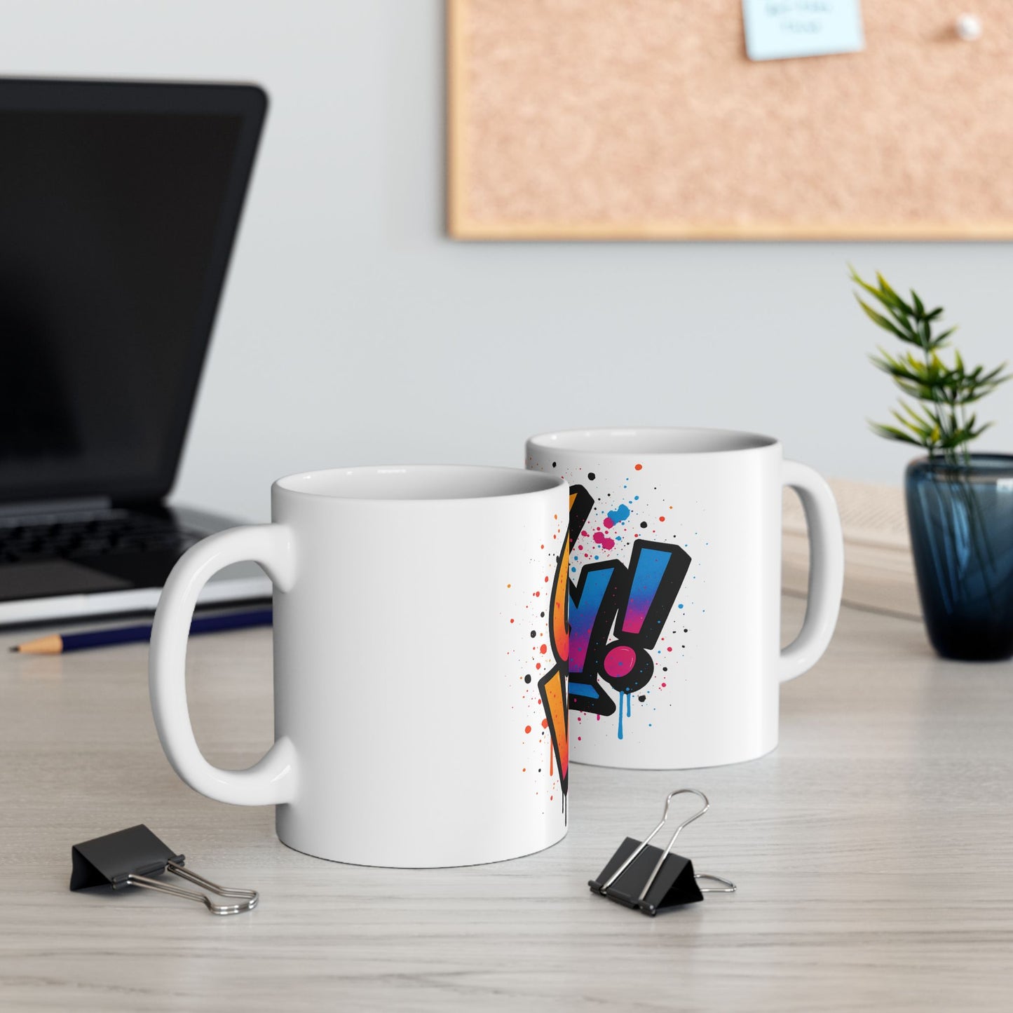 Two white mugs with colorful 'oy vey' designs on a desk with a laptop and office supplies.