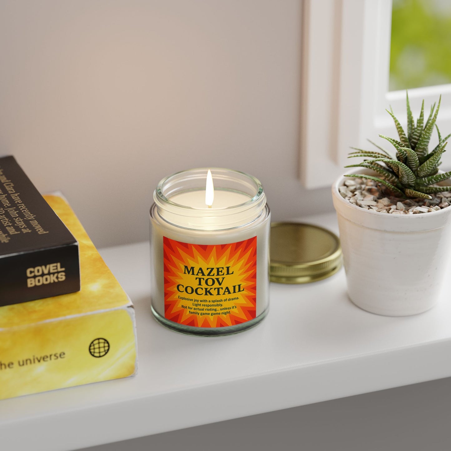 Candle labeled 'Mazel Tov Cocktail' on a shelf with books and a plant