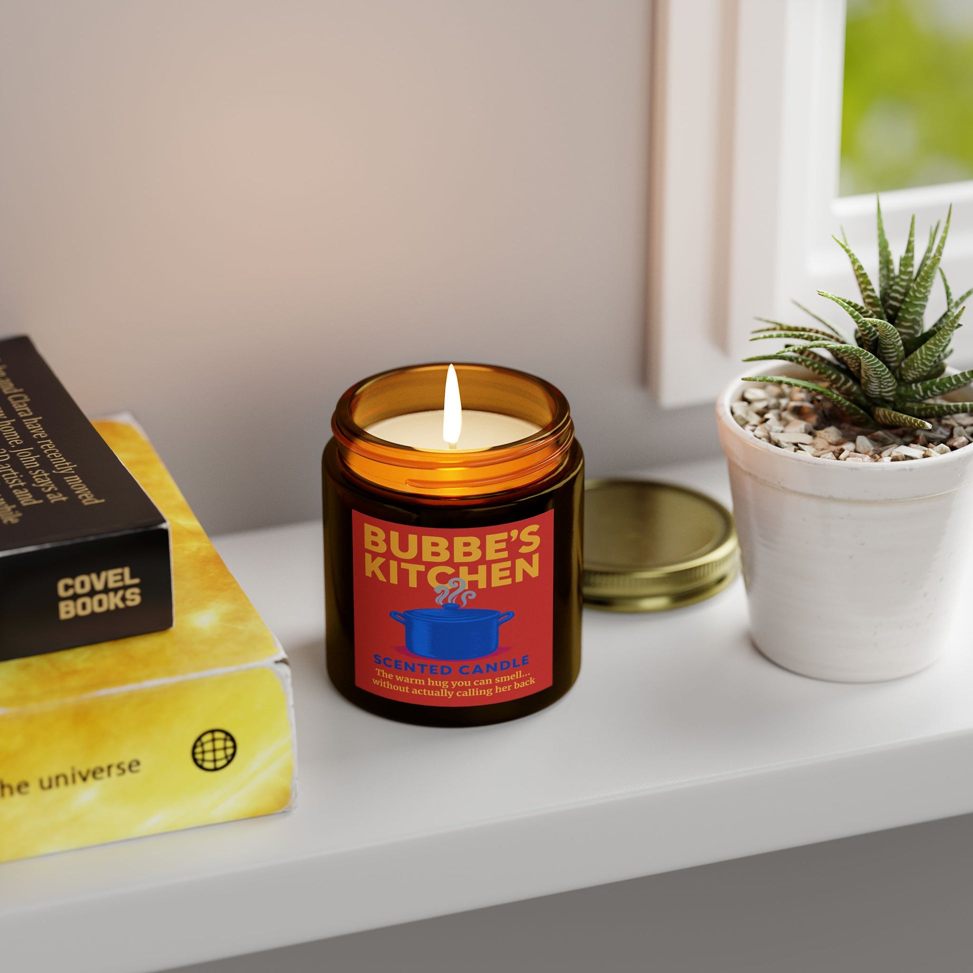 Candle labeled 'Bubbe's Kitchen' on a shelf with books and a plant