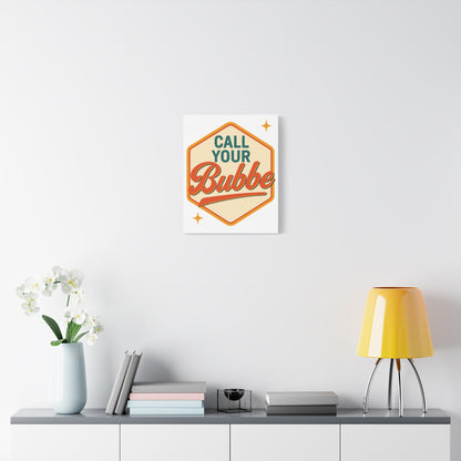 Decorative wall art with 'Call Your Bubbe' text on a white wall above a shelf with a lamp and books.
