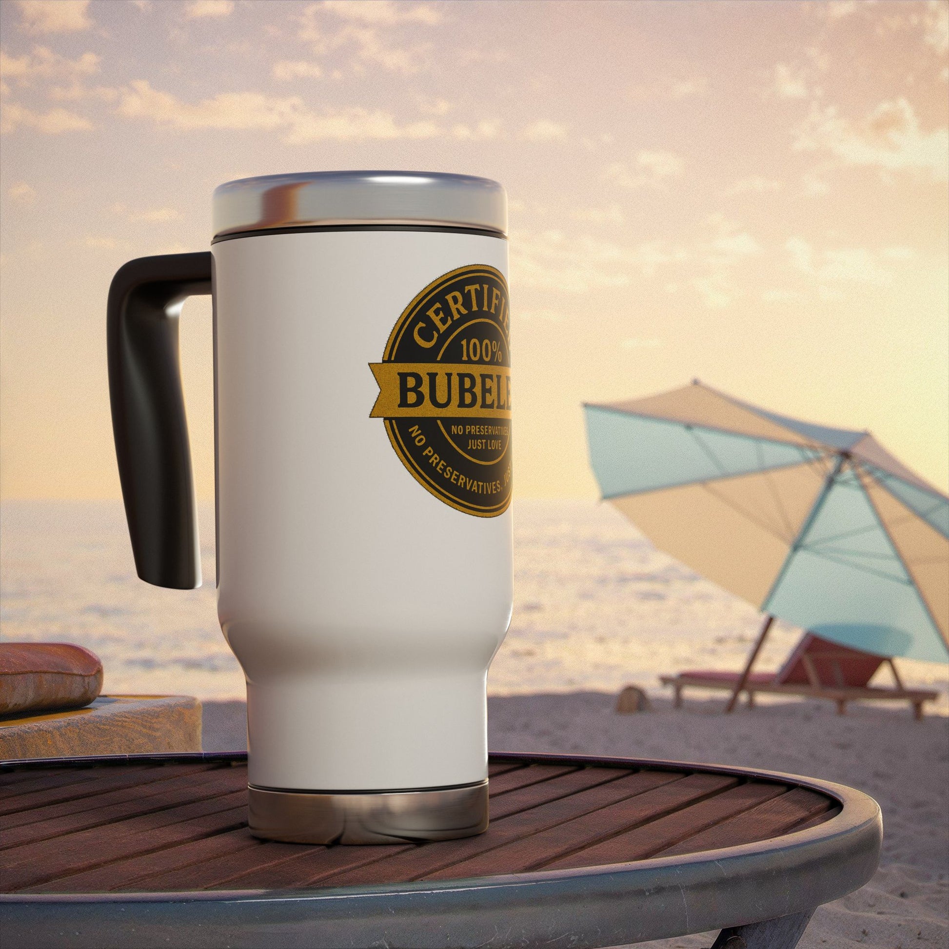 White travel mug with a gold 'certified bubeleh' label on a beach table with an umbrella and chairs in the background.