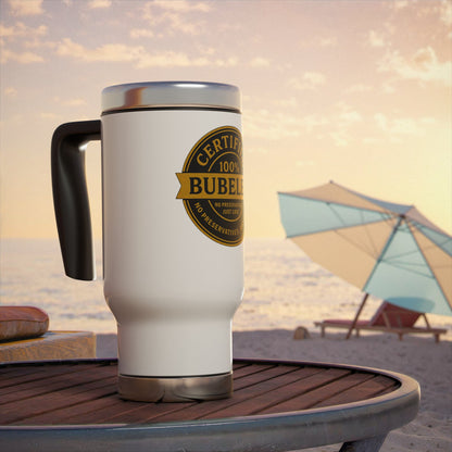 White travel mug with a gold 'certified bubeleh' label on a beach table with an umbrella and chairs in the background.