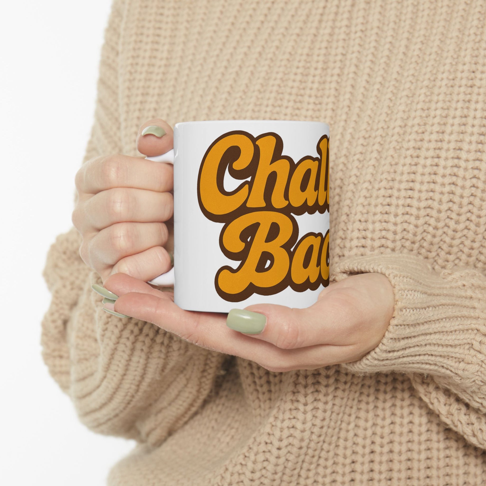 Person holding a mug with 'Challah Back' text in yellow and brown, wearing a beige sweater.