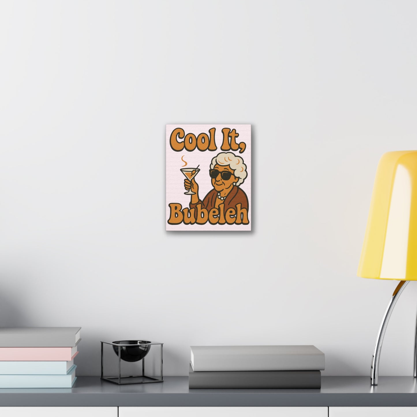 Decorative wall art with a vintage-style illustration of a woman holding a cocktail, text 'Cool It, Bubeleh', on a white wall.