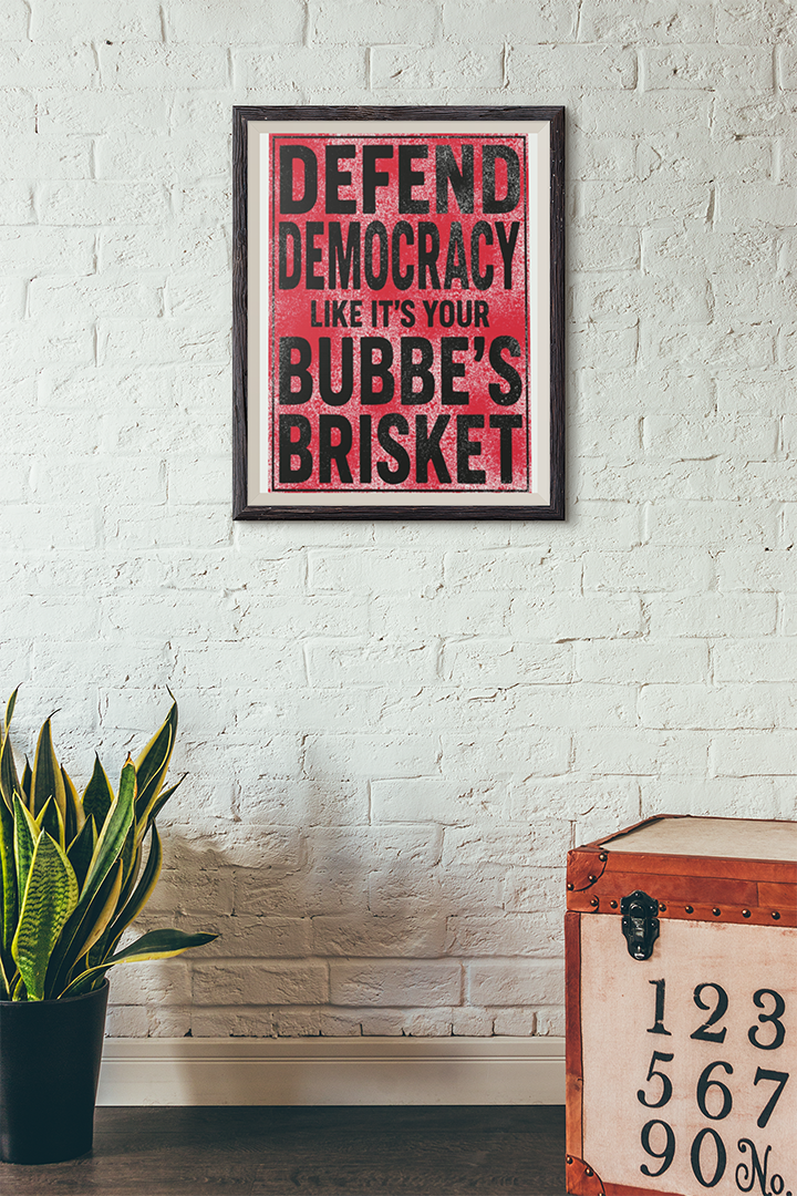 Framed poster with text on a white brick wall, next to a plant and wooden chest.