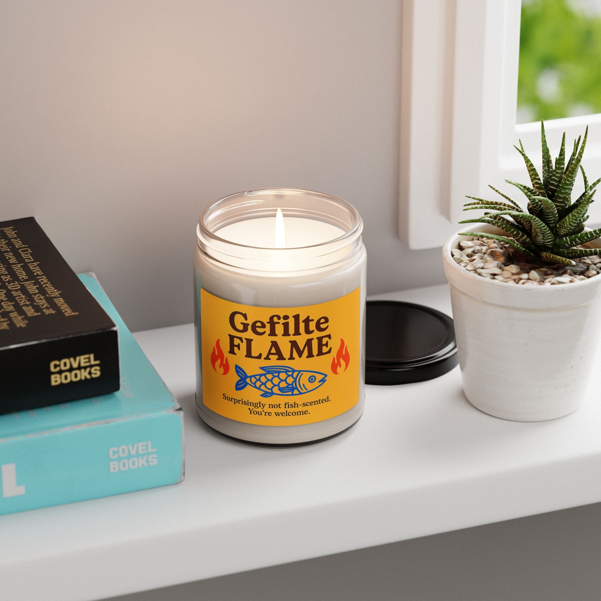 Candle labeled 'Gefilte Flame' on a shelf with books and a plant