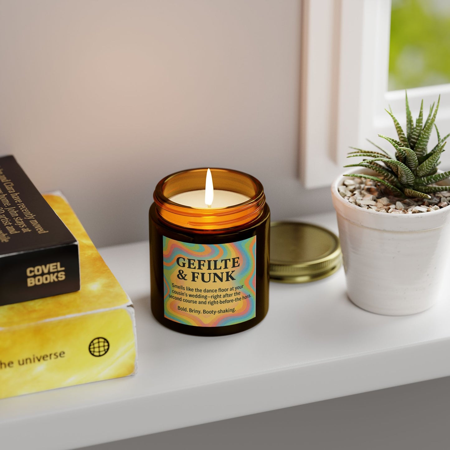 Candle labeled 'Gefilte & Funk' on a shelf with books and a plant