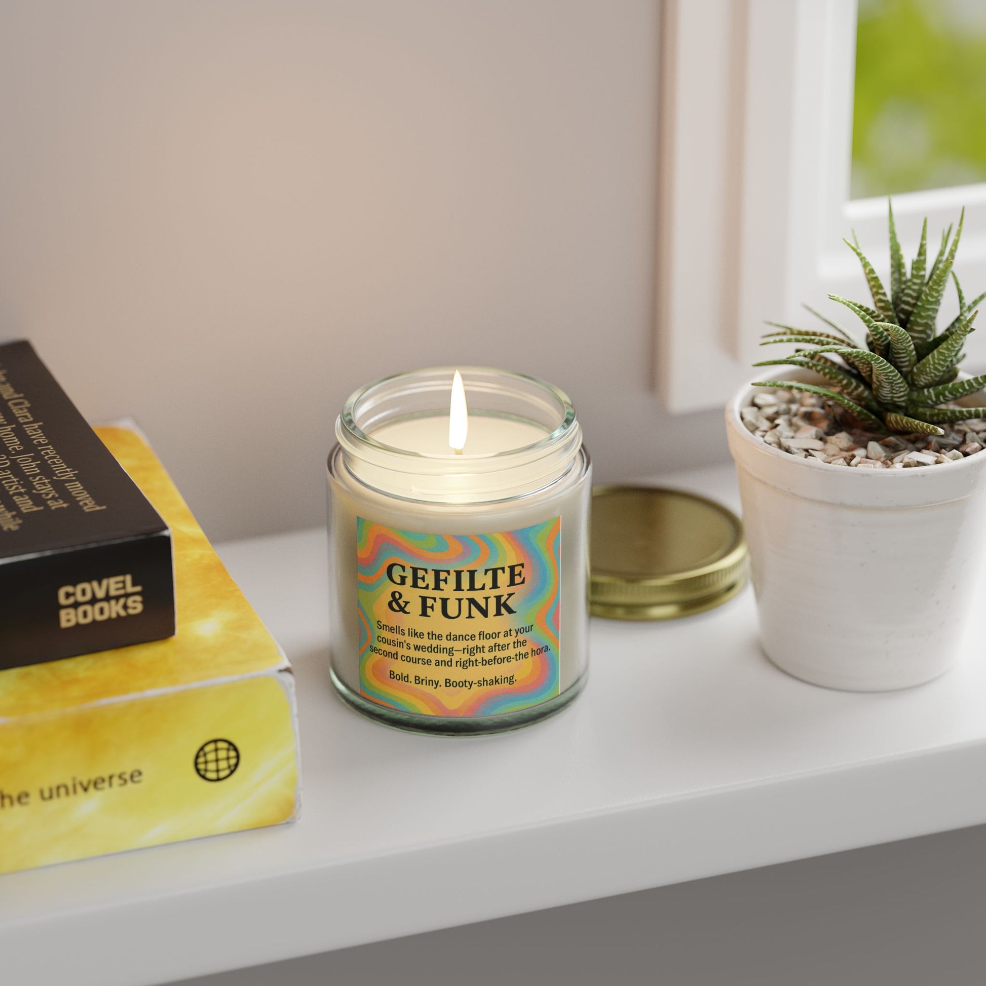 Candle labeled 'Gefilte & Funk' on a shelf with books and a plant