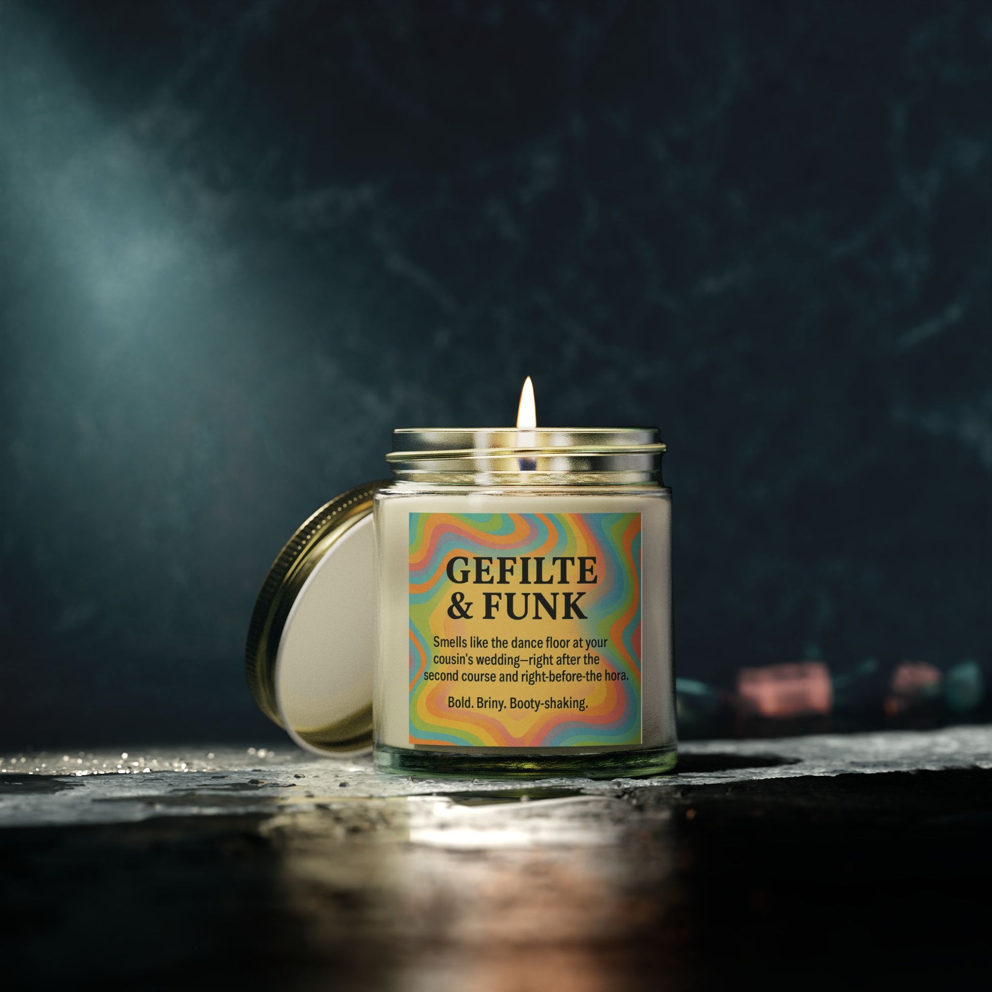 Candle in a jar labeled 'Gefilte & Funk' with a colorful label on a dark background.