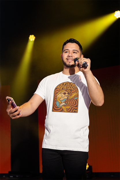 Man on stage holding a microphone and phone with a graphic t-shirt, illuminated by stage lights.