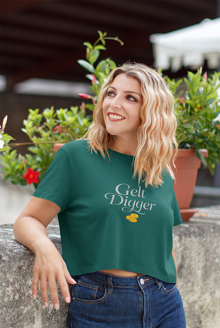 Woman wearing a green t-shirt with 'Gelt Digger' text, standing outdoors with plants in the background.