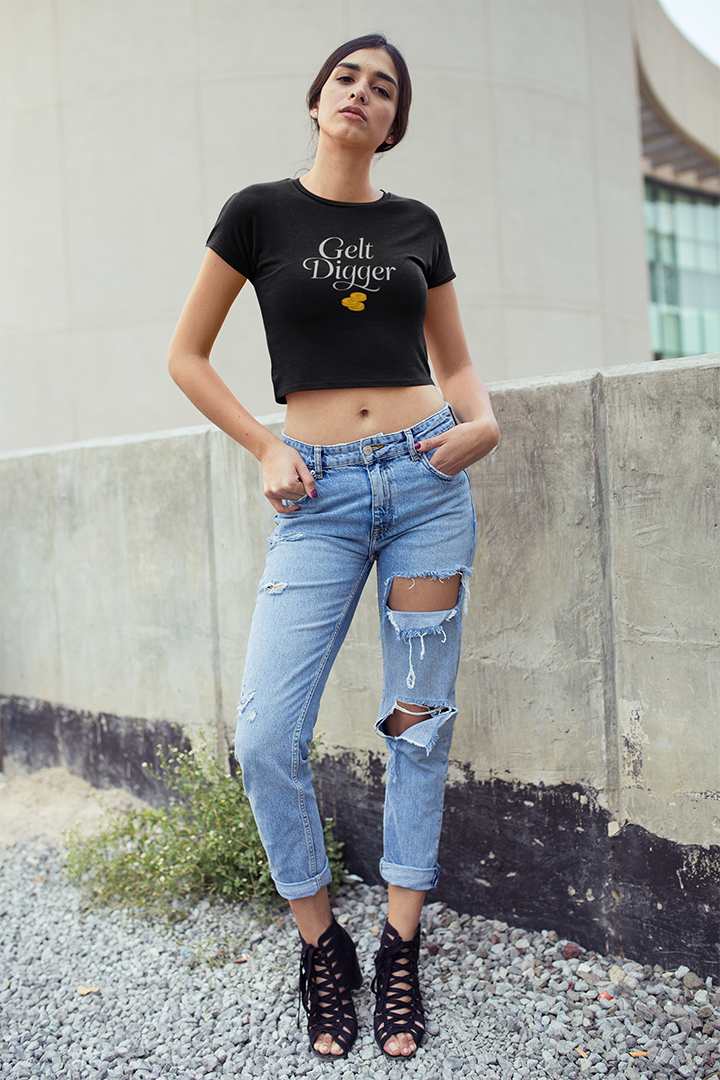 Woman wearing a black t-shirt with text and ripped jeans standing against a concrete wall.