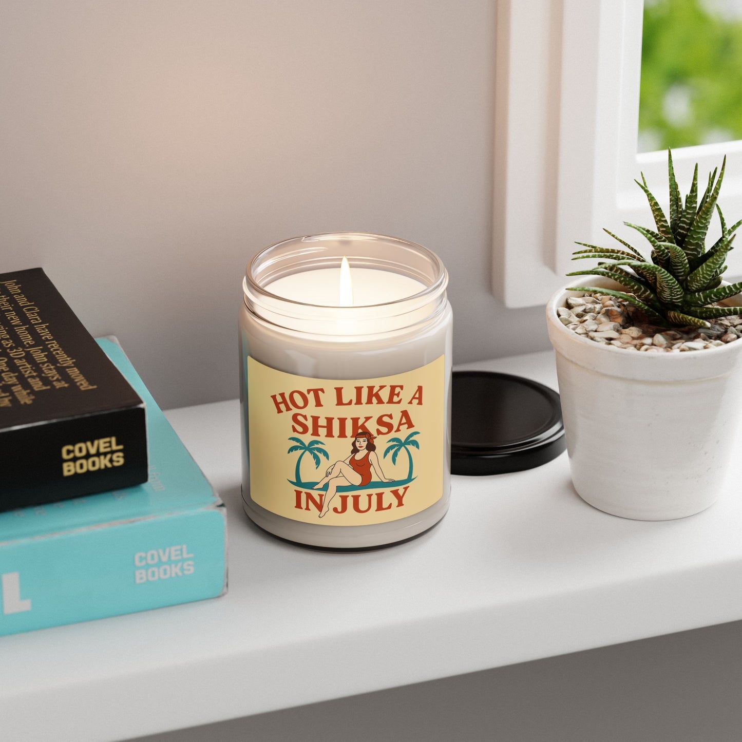 Candle with a humorous label on a shelf with books and a plant