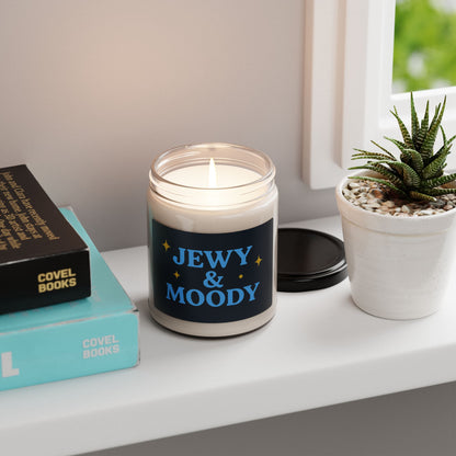 Candle with 'JEWY & MOODY' label on a shelf with books and a plant