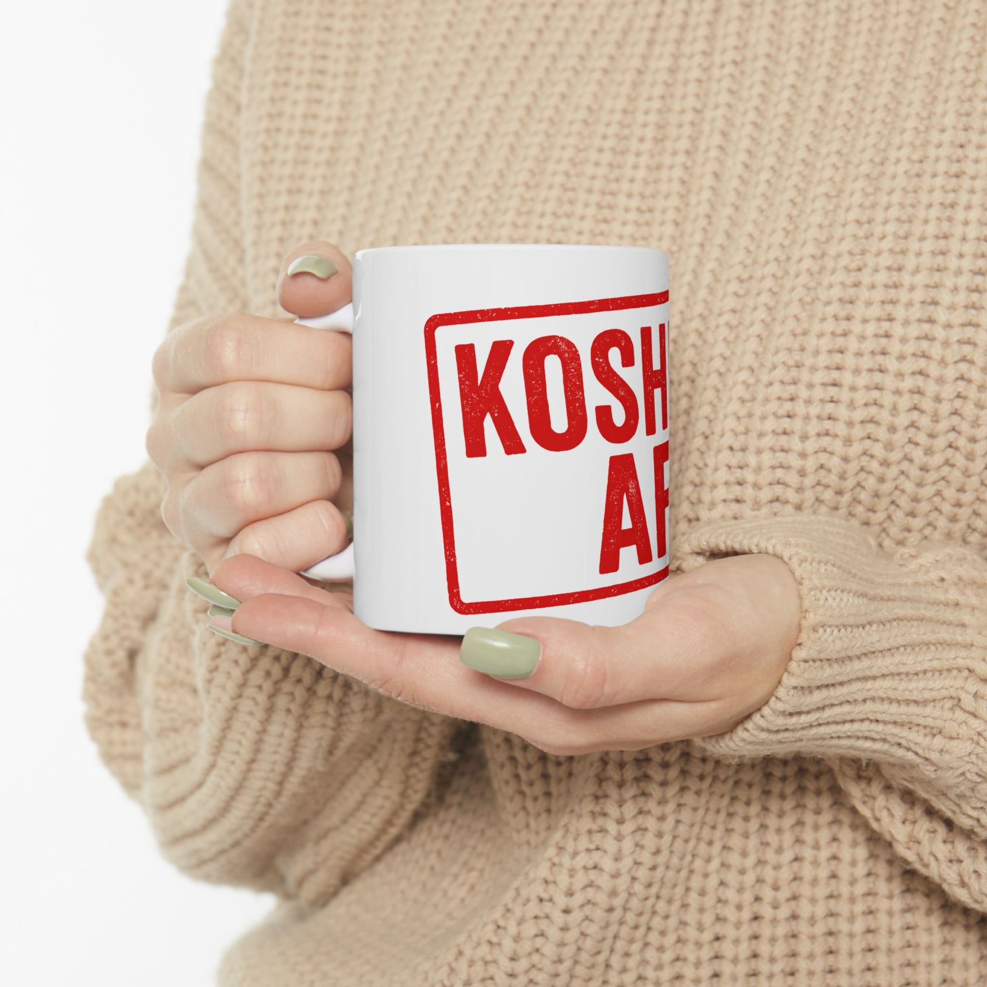 Person holding a white mug with 'kosher af' printed in red on a beige background
