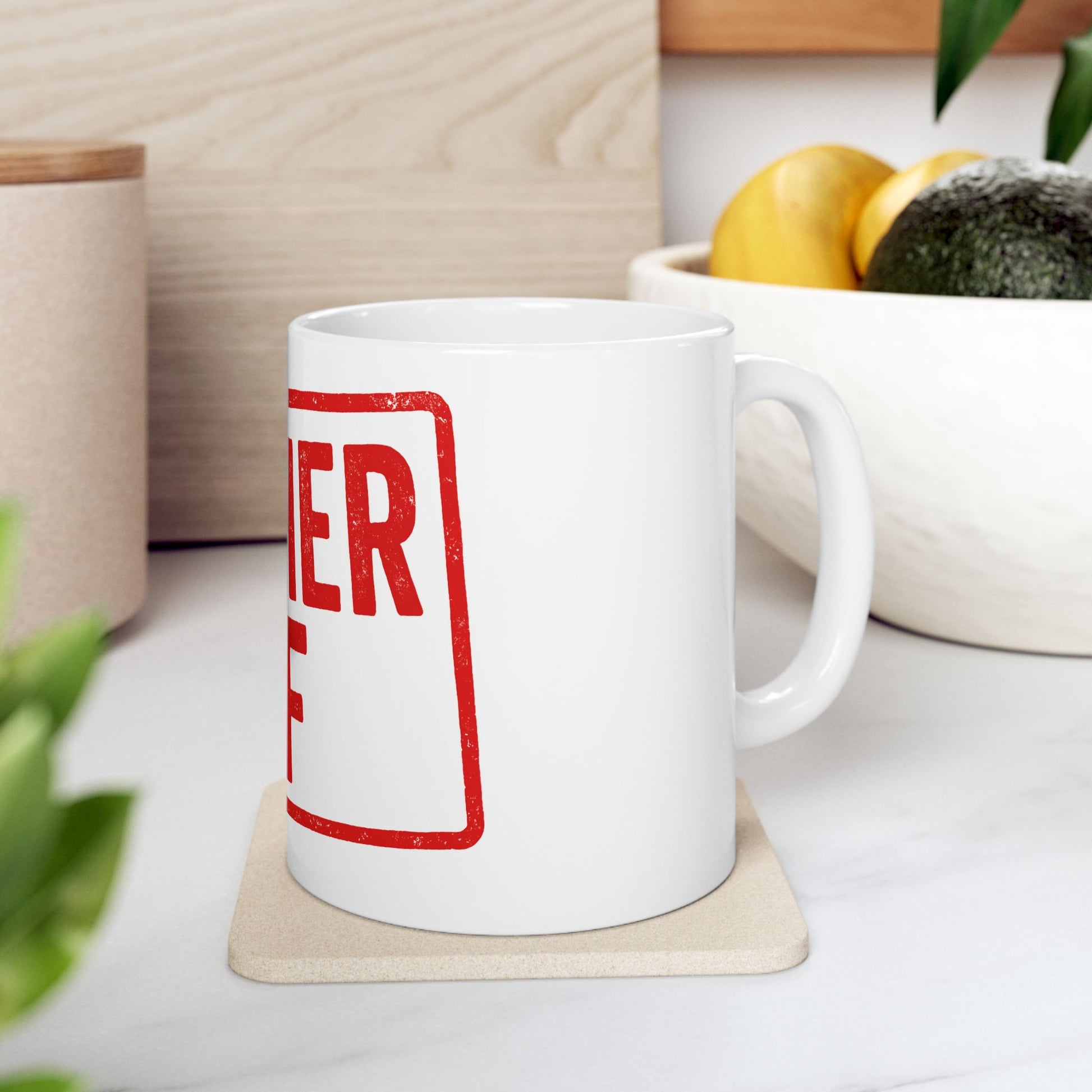 White mug with 'kosher af' in red text on a coaster, placed on a surface with a plant and container in the background.