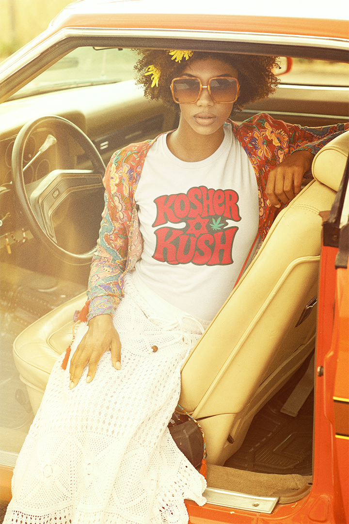 Woman sitting in a car wearing a 'Kushier than Kush' shirt with a retro vibe.