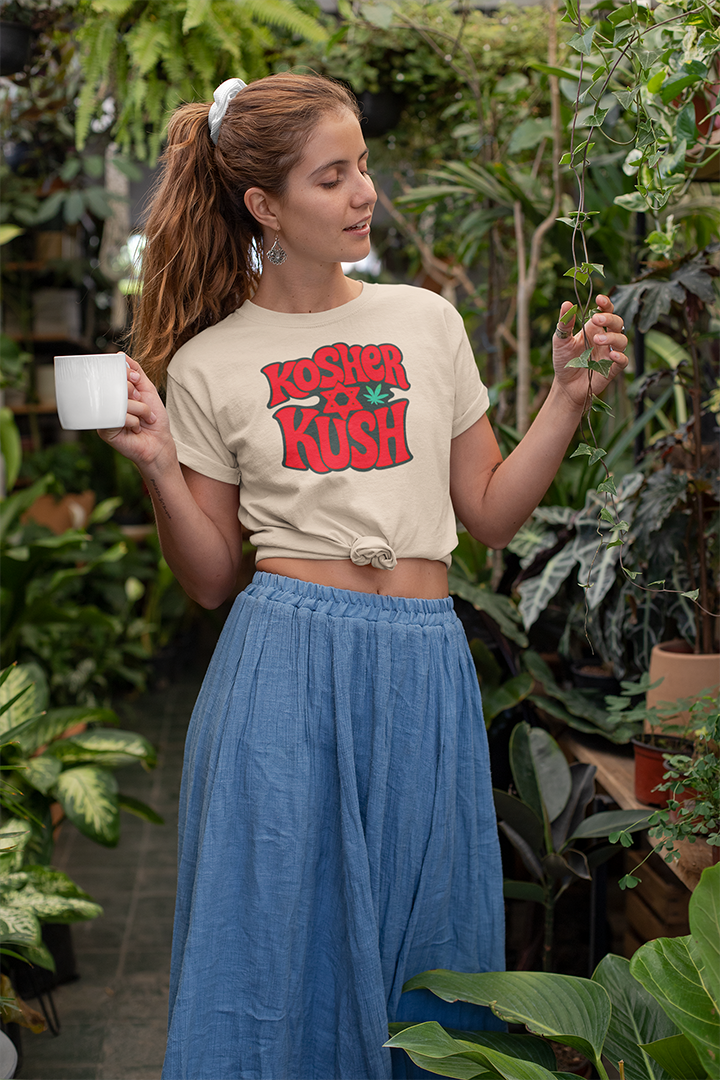 Woman holding a cup and a plant, wearing a 'Kosher Kush' shirt in a garden setting