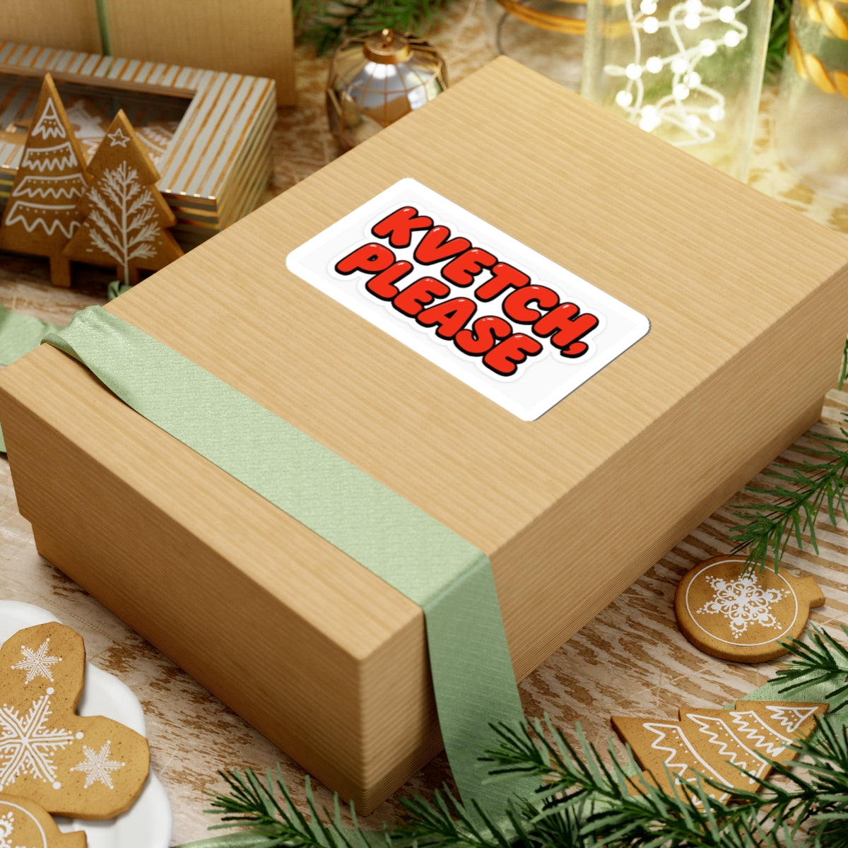 Wooden gift box with a green ribbon and 'Kvetch Please' sticker, surrounded by Christmas decorations.