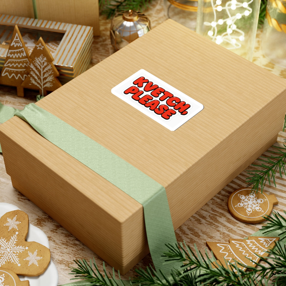 Wooden gift box with a green ribbon and 'Kvetch Please' sticker, surrounded by Christmas decorations.