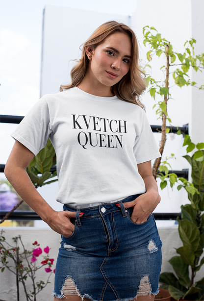 Woman wearing a white t-shirt with 'KVETCH QUEEN' text, standing outdoors with plants in the background.