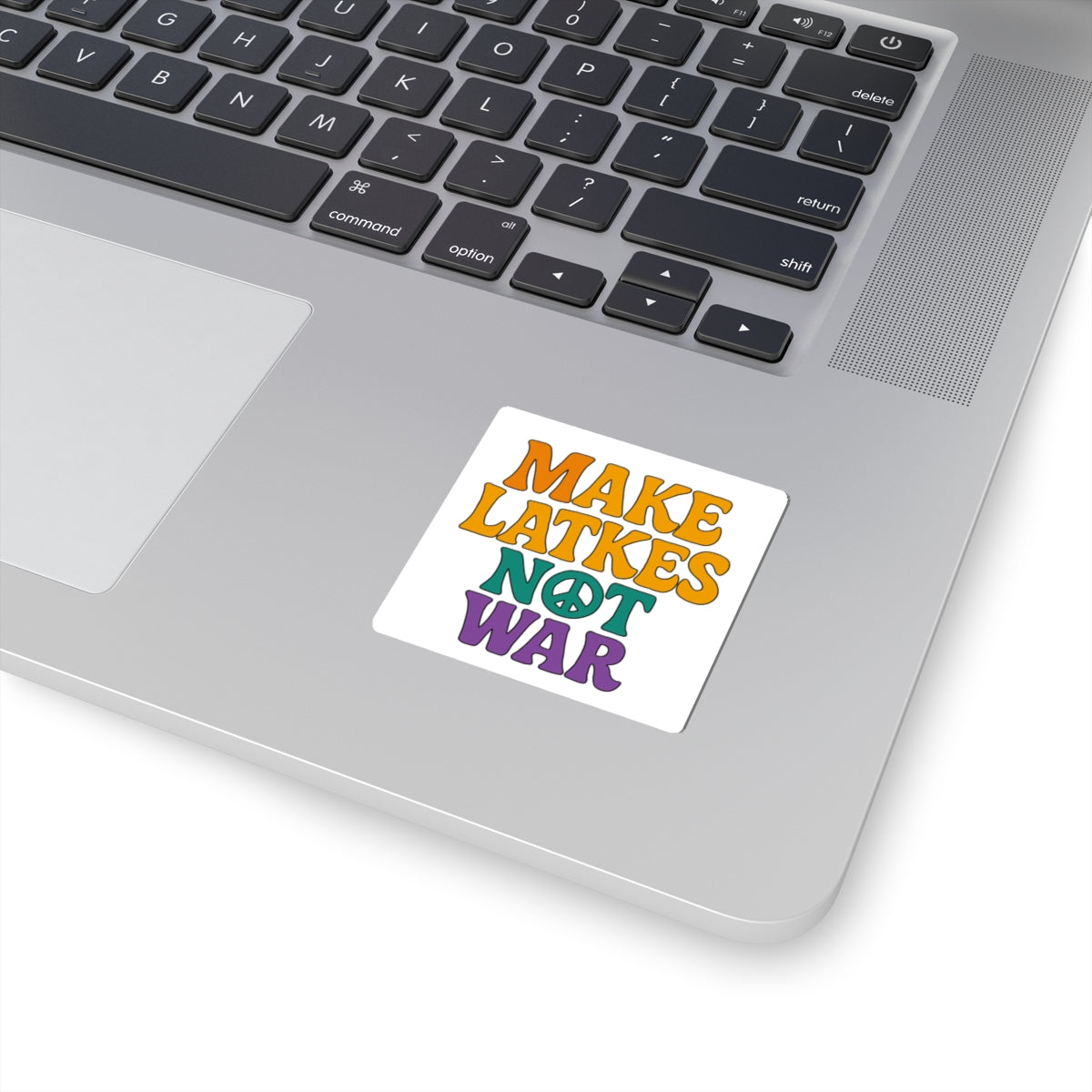 Laptop with a colorful sticker reading 'MAKE LATKES NOT WAR' on a white surface.