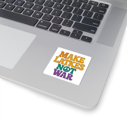 Laptop with a colorful sticker reading 'MAKE LATKES NOT WAR' on a white surface.
