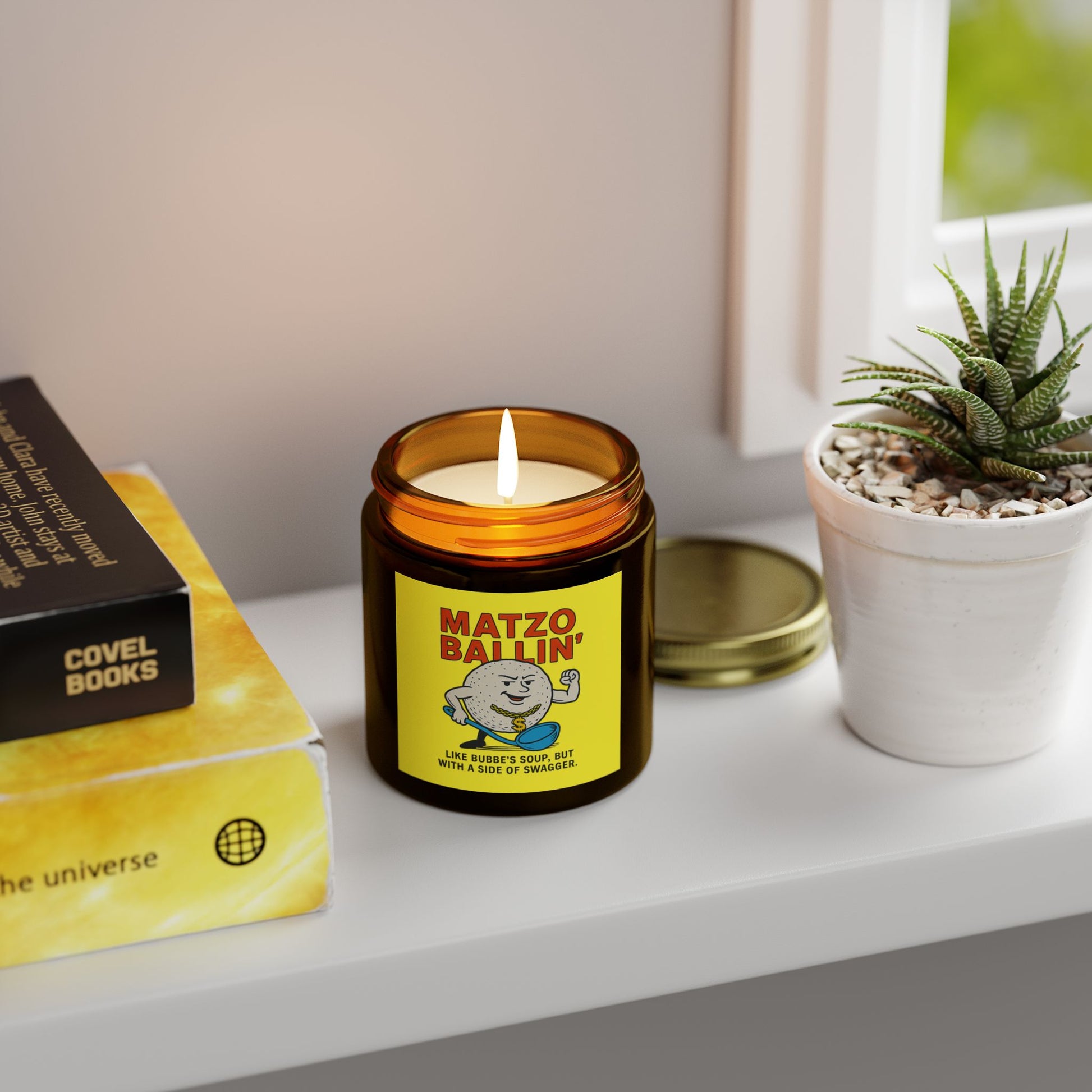 Candle labeled 'Matzo Ballin'' on a shelf with books and a plant