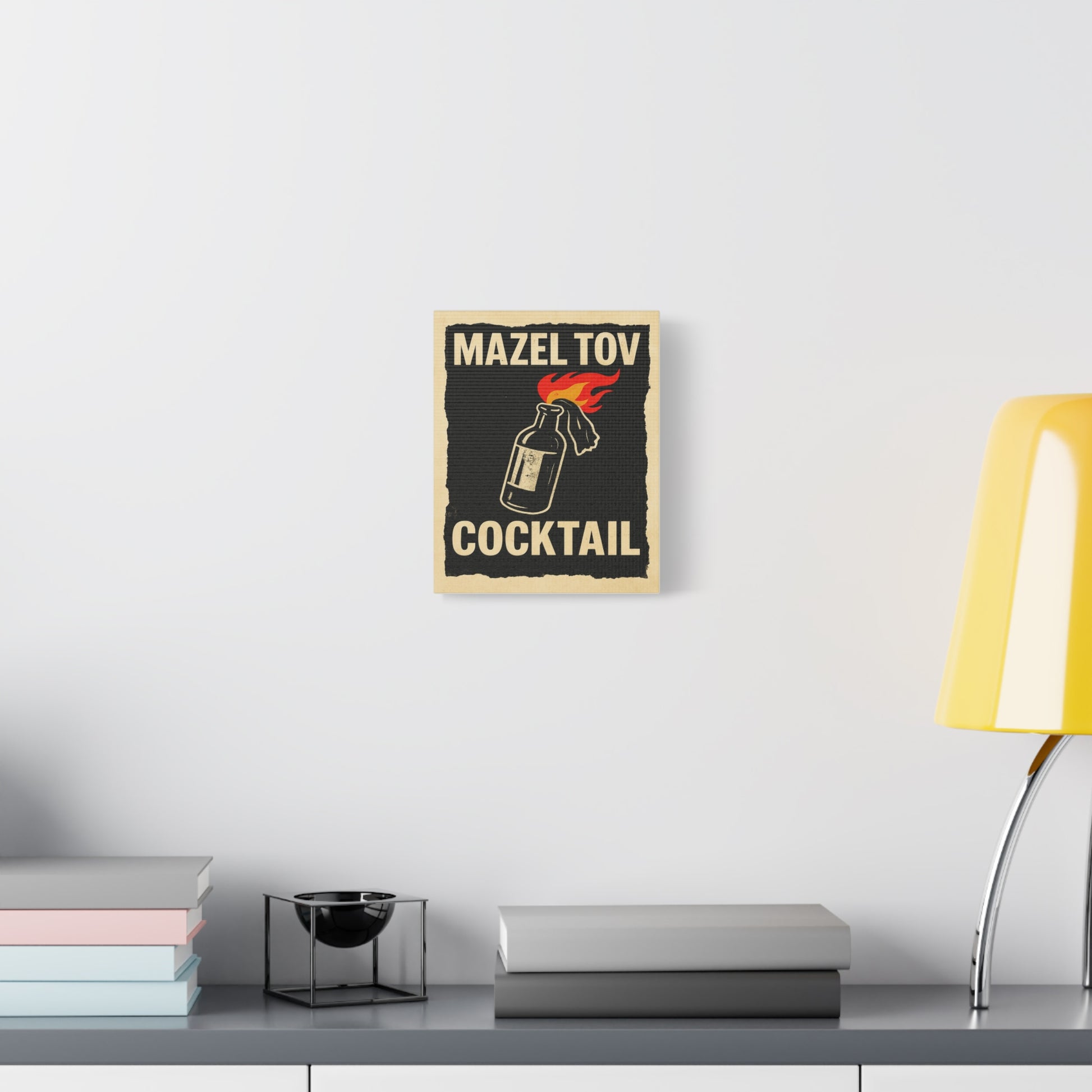 Poster with 'Mazel Tov Cocktail' design on a wall above a desk with books and a lamp.